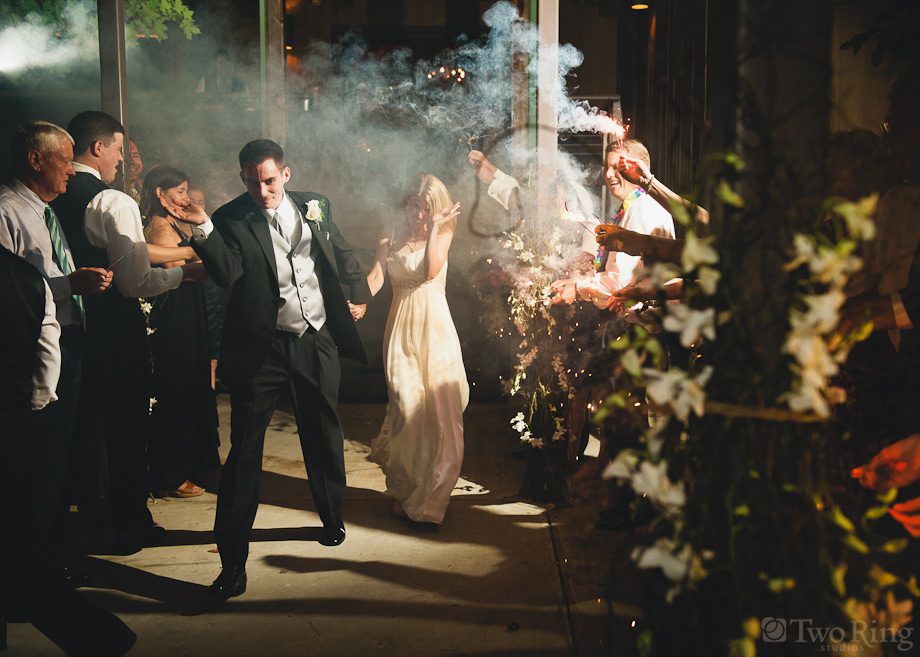Bride and groom exit wedding reception with sparkler smoke